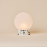 Oplaadbare tafellamp Metsu Small Arabescato wit marmer met glazen bol op beige achtergrond