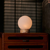 Cordless table lamp Metsu Small with Calacatta Vionaro pink marble base beside a picture frame
