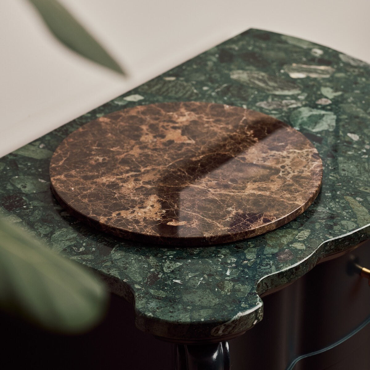 Emperador Dark marble tray resting on a scalloped green marble table beside a plant