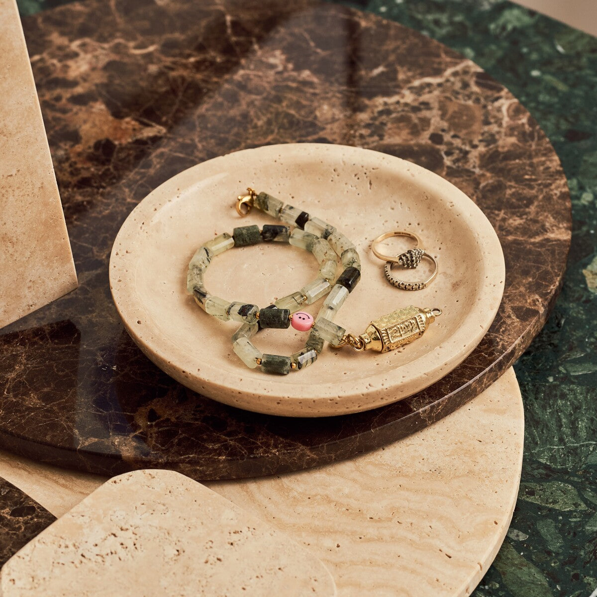 Round travertine dish with jewelry displayed beside the Emperador Dark marble tray