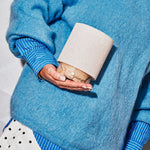 Rechargeable table lamp Tavellio Onoda Small held in one hand, showing its compact size, blue mohair sweater behind.