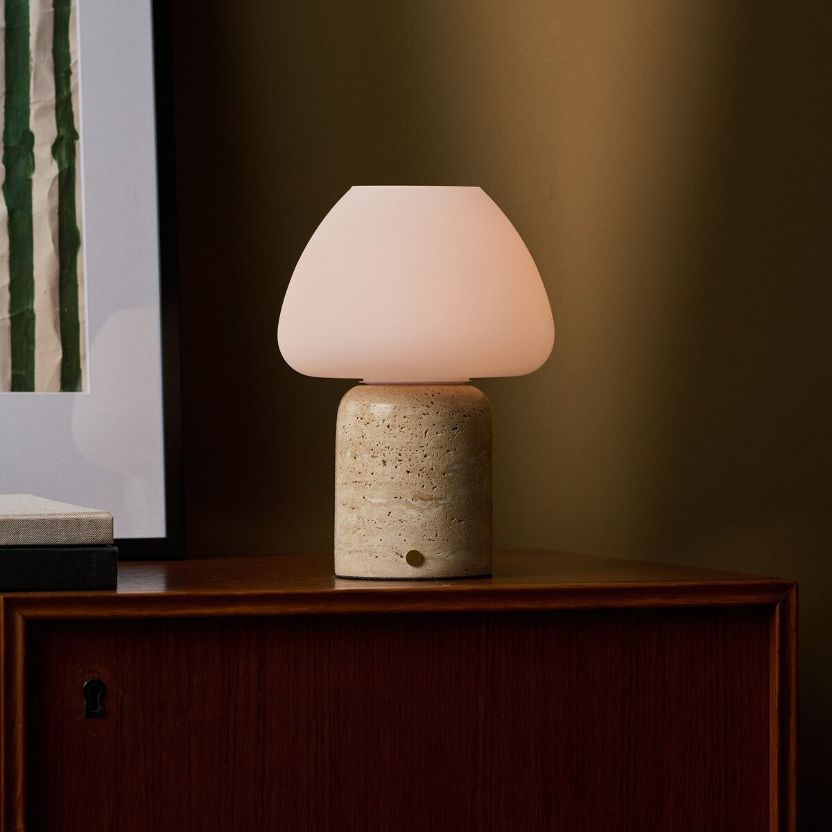 Oplaadbare tafellamp Ostade in beige travertin, warm lichtgevend naast een ingelijste foto