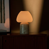 Tafellamp oplaadbaar Ostade, beige travertin voet met witte glazen kap op een houten dressoir