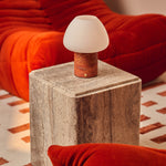 Oplaadbare tafellamp Ostade met Red Travertine marmeren voet op boekenstapel in woonkamer