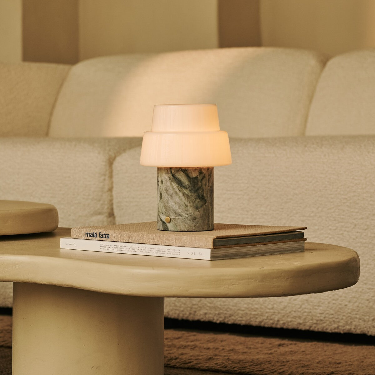 Tavellio Pissarro rechargeable table lamp in ice green marble lit atop stacked books on a coffee table.