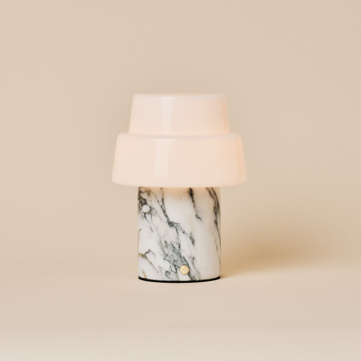 Cordless table lamp with two-tier opal glass shade and beige marble base under warm spotlight