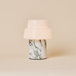 Cordless table lamp with two-tier opal glass shade and beige marble base under warm spotlight