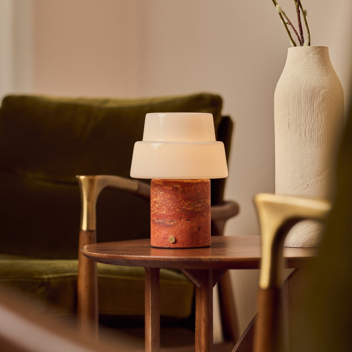 Cordless table lamp Pissarro Medium red travertine base on wooden side table beside green armchair