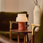 Cordless table lamp Pissarro Medium red travertine base on wooden side table beside green armchair