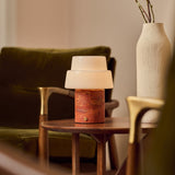 Cordless table lamp Pissarro Medium red travertine base on wooden side table beside green armchair