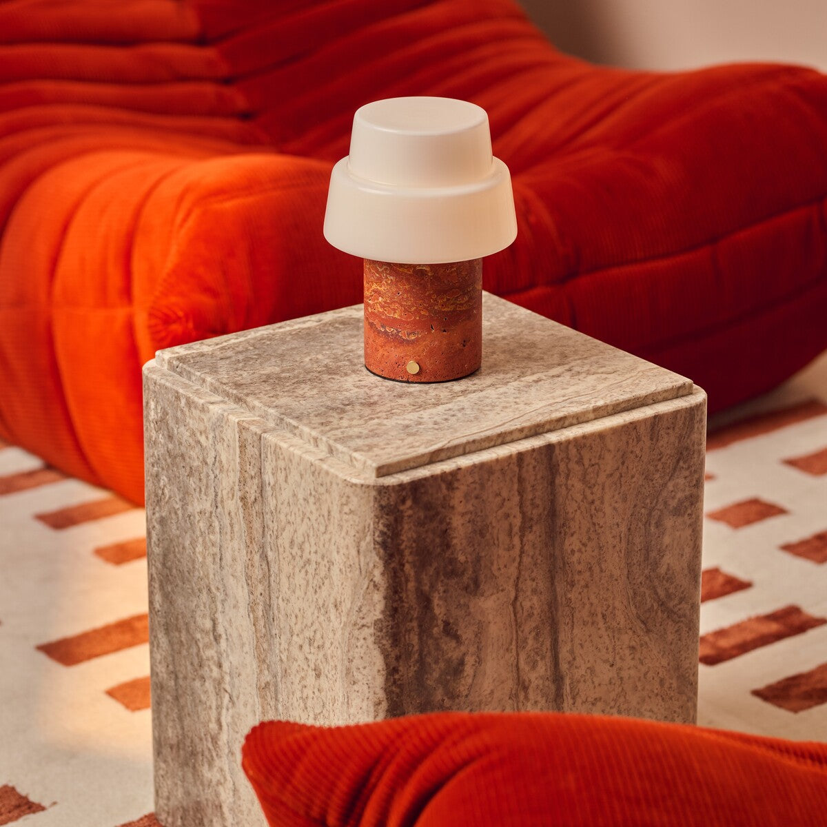 Rechargeable table lamp Pissarro Medium red travertine base on marble side table beside red sofa