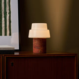 Cordless table lamp Pissarro Medium red travertine stone base with white bell glass shade on cabinet