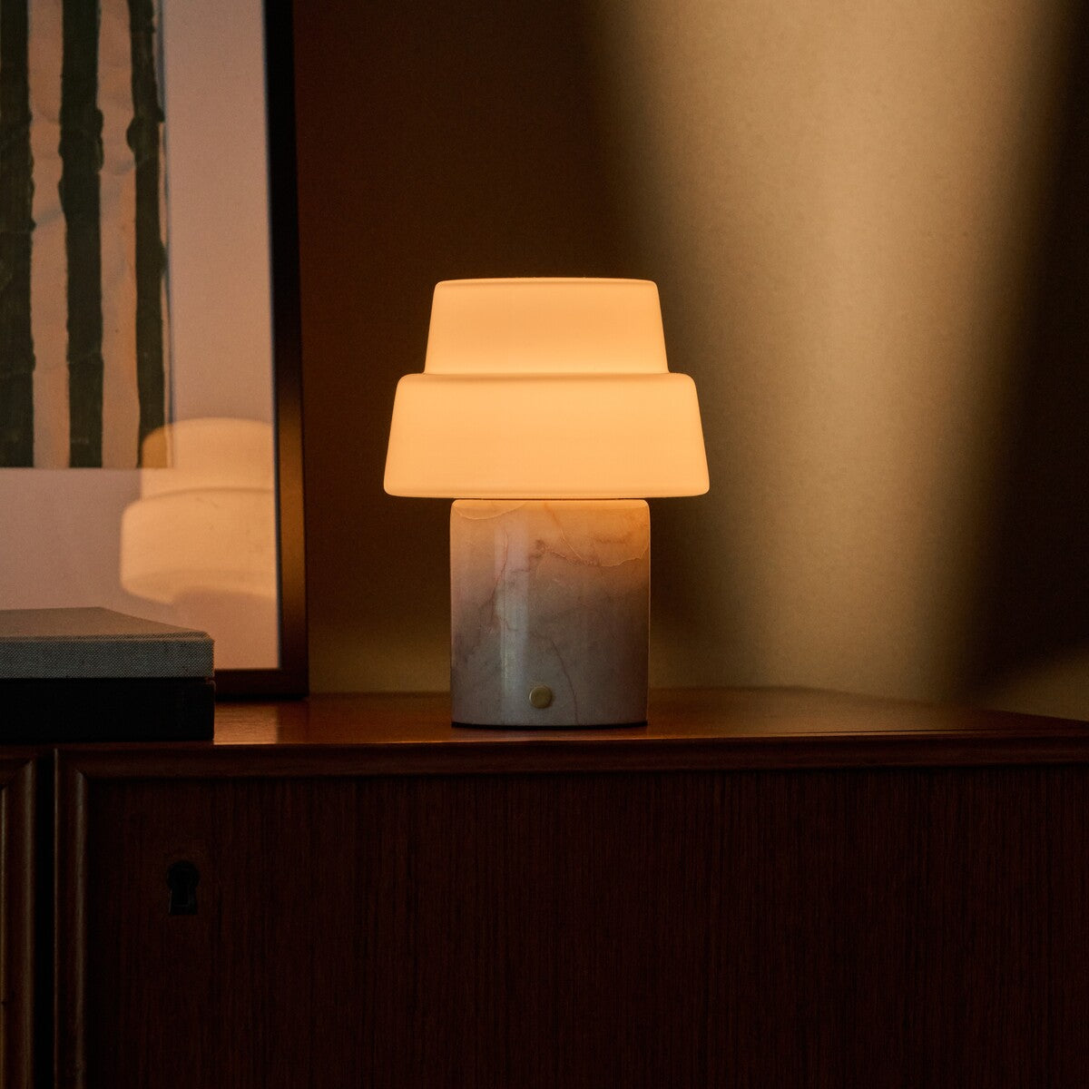 Cordless table lamp Pissarro in rosa aurora marble glowing on a dark wood cabinet