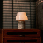 Pissarro rechargeable table lamp with silver travertine base and opal glass shade against striped blinds