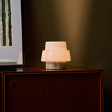 Oplaadbare tafellamp Pissarro Small zilver travertin op een houten dressoir in schemerlicht