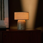 Redon Large cordless table lamp in beige travertine marble glowing on a wooden bedroom dresser