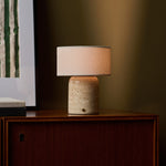 Redon cordless table lamp with beige travertine base and linen shade on wooden cabinet