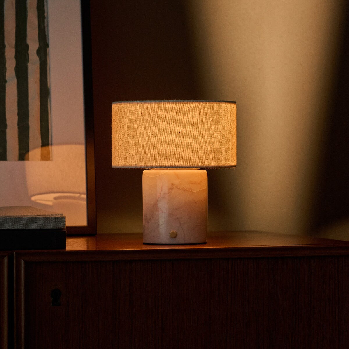 Redon rechargeable table lamp with rosa aurora marble base illuminated on a dark wood cabinet