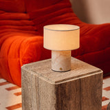 Redon cordless table lamp with rosa aurora marble base on a travertine side table by an orange sofa
