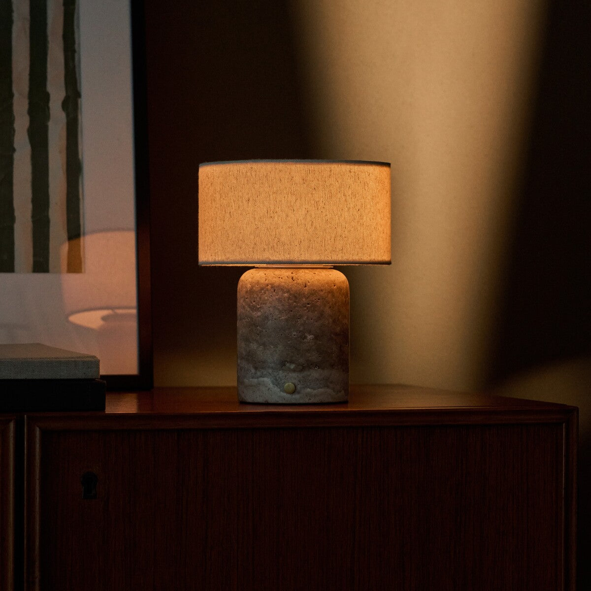 Redon cordless table lamp with silver travertine base and cream shade on wooden cabinet