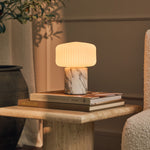 Renoir Medium cordless table lamp with arabescato marble base on a stack of interior books