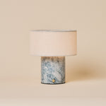 Cordless table lamp Redon with blue calcite marble base and ribbed opal glass shade on a dark coffee table