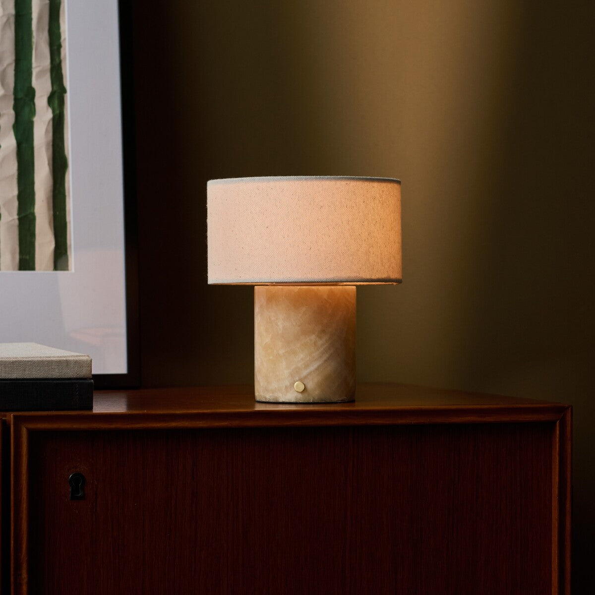 Redon rechargeable table lamp with honey onyx marble base beside framed art on a wood cabinet