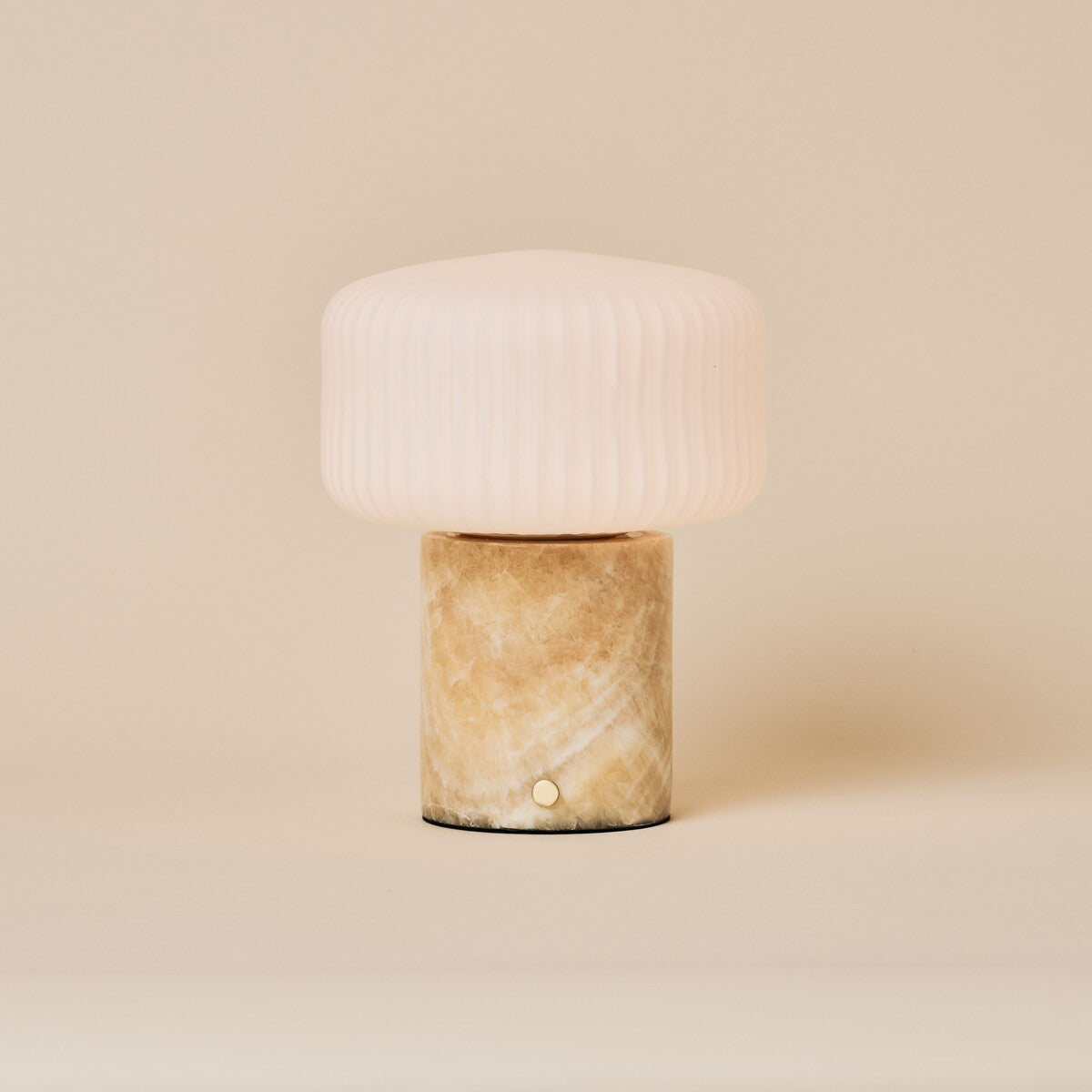 Renoir Medium cordless table lamp with honey onyx marble base beside a green velvet armchair