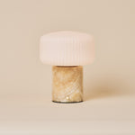 Renoir Medium cordless table lamp with honey onyx marble base beside a green velvet armchair