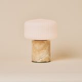 Renoir Medium cordless table lamp with honey onyx marble base beside a green velvet armchair