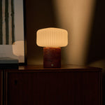 Rechargeable table lamp Renoir red travertine base with ribbed glass shade lit on a wooden cabinet