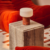 Cordless Renoir table lamp in red travertine with fluted glass shade on a stone side table