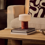 Rechargeable Renoir table lamp in red travertine with a ribbed white glass shade on books
