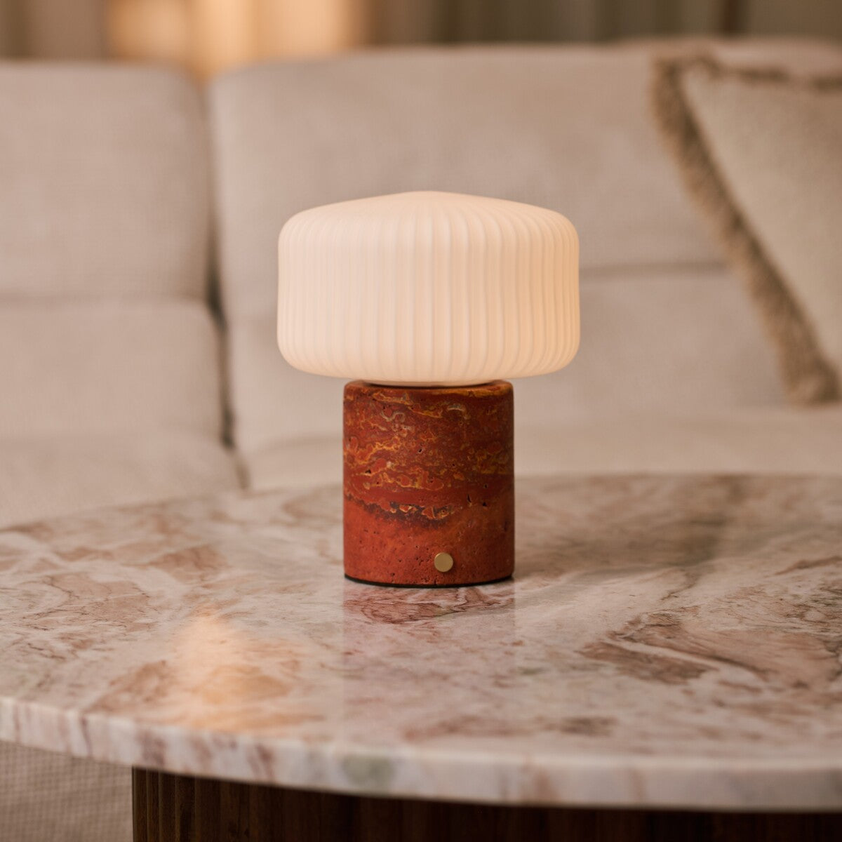 Cordless table lamp Renoir red travertine base with ribbed glass shade on a marble coffee table