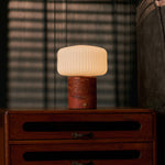 Cordless table lamp Renoir red travertine base with ribbed glass shade on a dark wood nightstand