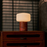Cordless table lamp Renoir red travertine base with ribbed glass shade on a dark wood nightstand