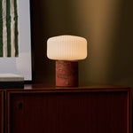 Cordless table lamp Renoir red travertine base with ribbed glass shade beside a framed art print