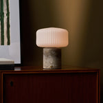 Rechargeable Renoir table lamp in silver travertine with ribbed shade beside a red sofa