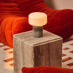 Rechargeable Renoir table lamp in silver travertine with ribbed shade on a sideboard