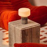Rechargeable Renoir table lamp in silver travertine with ribbed shade on a sideboard