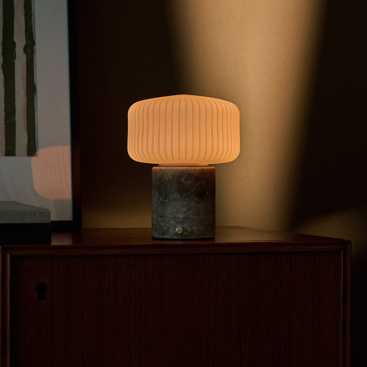 Rechargeable table lamp Renoir grey silver travertine base with ribbed glass shade on a wood cabinet