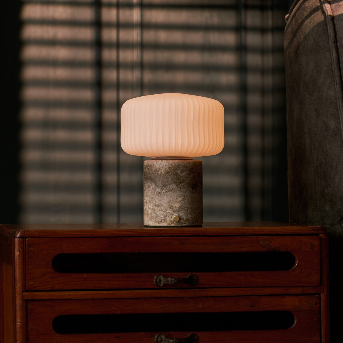 Cordless Renoir table lamp in silver travertine with fluted glass shade on a dresser