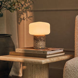 Cordless Renoir table lamp in silver travertine with a fluted glass shade on stacked books