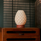 Rechargeable table lamp Serena red travertine porcelain shade glowing on wooden cabinet