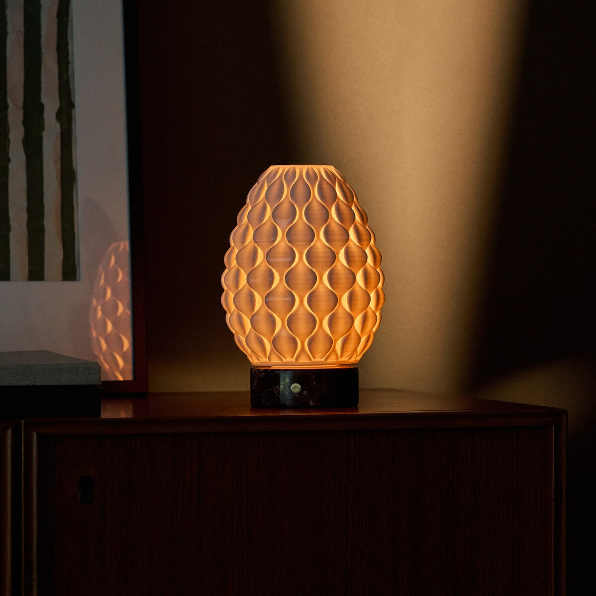 Serena Rosso Levanto cordless table lamp glowing on a cabinet beneath green striped wall art