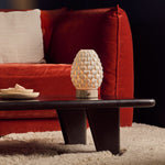 Cordless table lamp Serena silver travertine porcelain shade glowing on dark table by red sofa