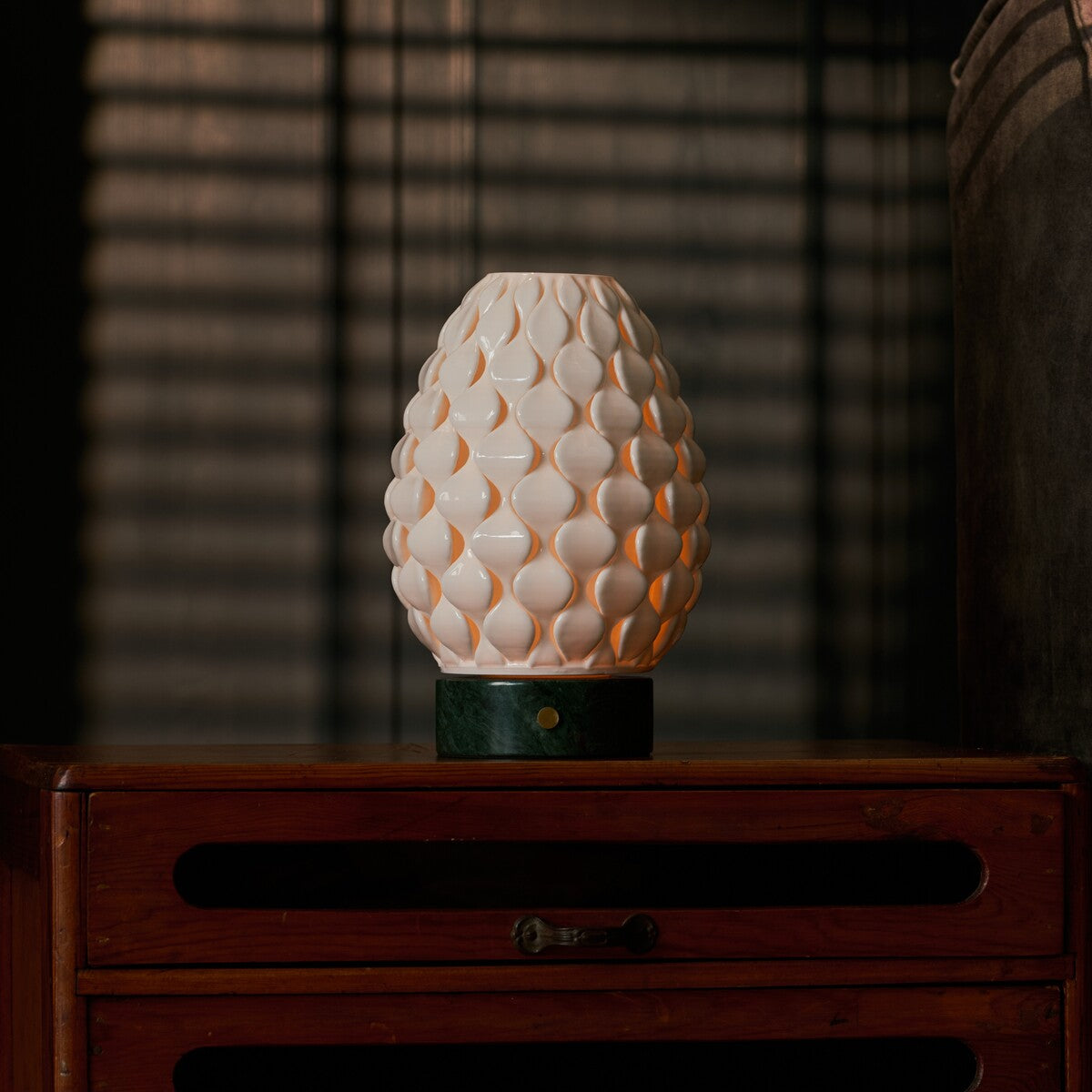 Serena Verde Alpi cordless table lamp glowing on a dark wood dresser in a striped-blind bedroom