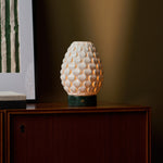 Serena Verde Alpi cordless table lamp glowing on a cabinet beneath green striped wall art