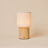 Dick bois marron clair lampe de table sans fil Tavellio – fond studio beige – abat-jour cylindrique en lin