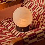 Tafellamp oplaadbaar Flore Small donkerbruin hout met glazen bolkap op een patroonstof fauteuil